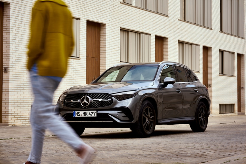 Ein dunkelgrauer Mercedes-Benz SUV Mietwagen parkt an einer Straße. Im Vordergrund überquert eine Person die Straße.